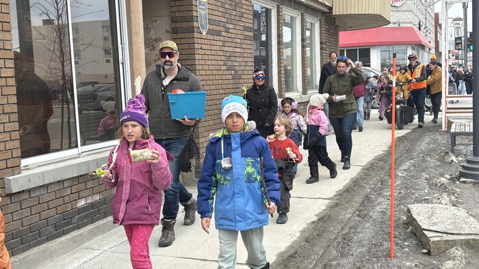 Plusieurs personnes, dont des enfants, marchent sur un trottoir.    