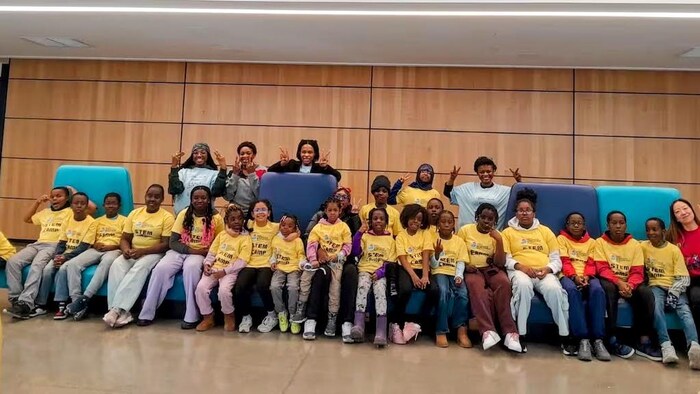 Des dizaines d’enfants et quelques membres du personnel de l’Initiative pour le développement de la petite enfance posent pour une photo de groupe dans un atrium, assis sur des canapés.