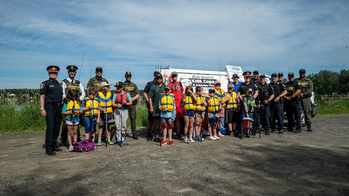 Un groupe d'enfants, des membres du Service de police du Grand Sudbury et de la Police provinciale de l’Ontario, ainsi que des agents de conservation du ministère des Richesses naturelles et des Forêts de l'Ontario posent pour une photo.