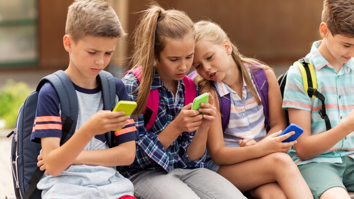 Des enfants portant des sacs d'école utilisent des téléphones cellulaires.