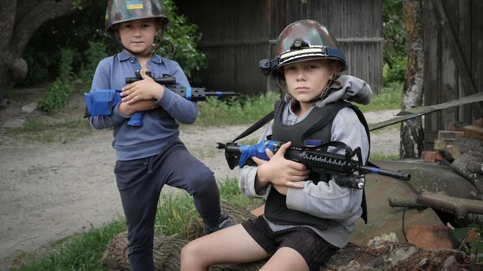 Deux jeunes garçons ukrainiens jouent aux soldats portant un casque et un fusil.