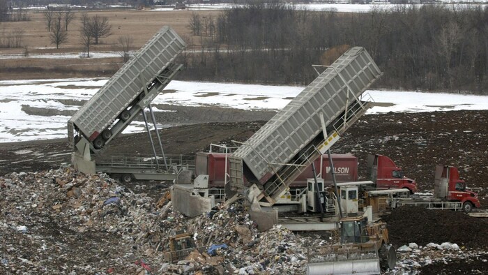 Deux camions à benne déposent des déchets sur un immense terrain.