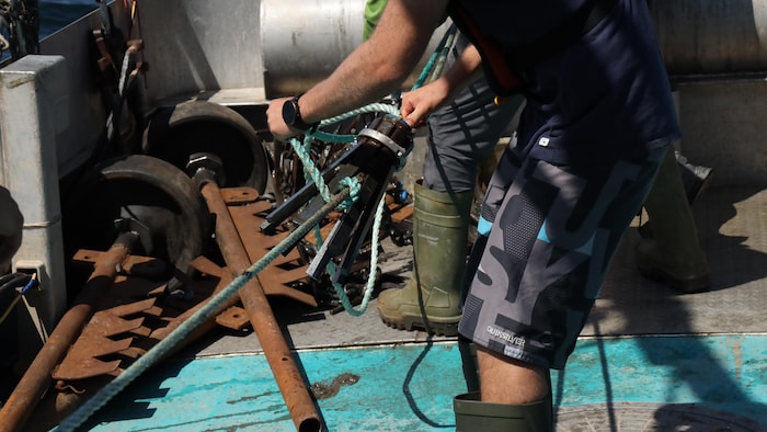Un homme manipule un grappin et des cordages à bord d'un bateau.