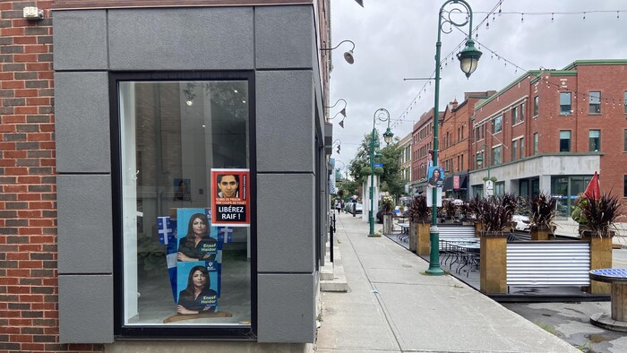 Du mobilier urbain dans la rue et trois affiches collées sur une vitre d'un local commercial.
