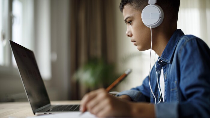 Un adolescent, qui écoute de la musique, fait ses devoirs en ligne.