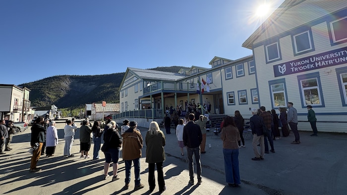 Des personnes dans la rue devant un bâtiment de l'Université du Yukon à Dawson regardent des personnes en train de signer des papiers.