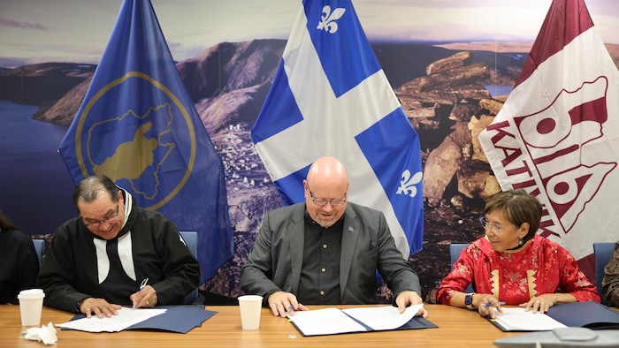 Trois personnes signent une entente assises à un bureau. 
