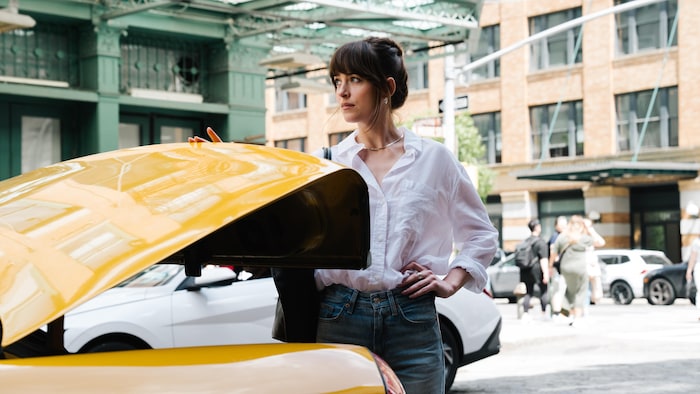 Une femme brune ferme le coffre d'une voiture jaune.