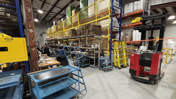 Une personne travaille dans un large entrepôt rempli de boîtes et de matériel. 