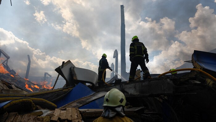 Des pompiers travaillent à éteindre un incendie dans les débris d'un entrepôt.