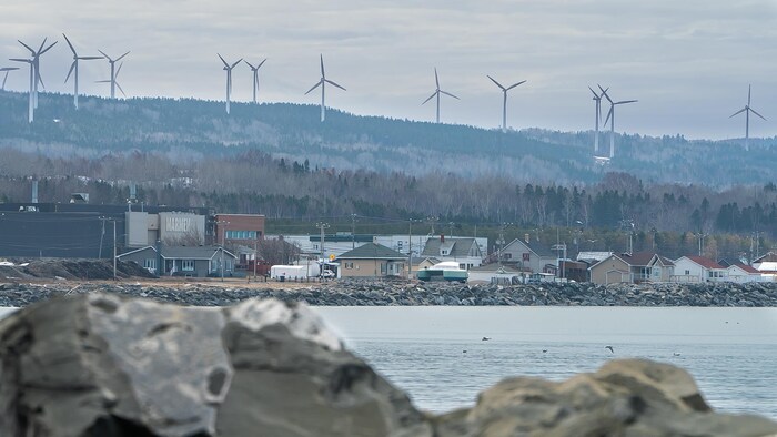 Une entreprise aux abords du fleuve Saint-Laurent. Des éoliennes surplombent l'entreprise.