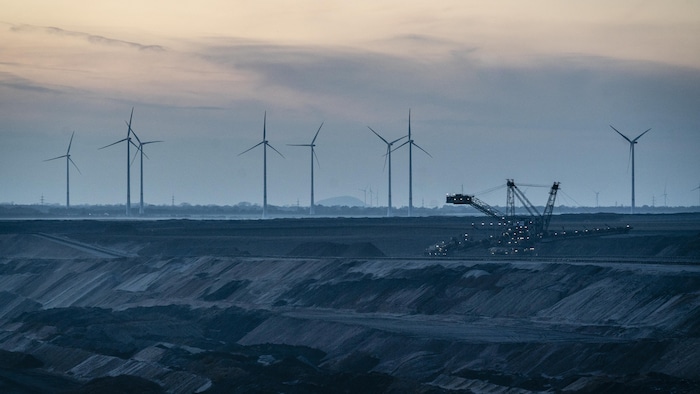 Une pelleteuse travaille dans une mine de lignite. À l'arrière-plan se trouvent des éoliennes. 