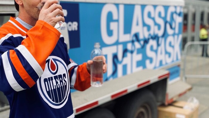 Un partisan des Oilers boit un verre d'eau devant un réservoir mobile d'eau potable, situé à côté de la place Rogers à Edmonton.