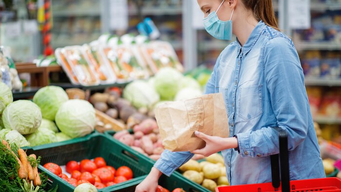 Une femme choisit ses légumes dans une allée d'épicerie. Elle porte un masque. 