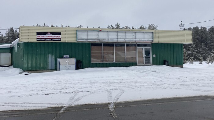 Une bâtisse vide aux fenêtres placardées sur laquelle est installée une affiche « à vendre ».