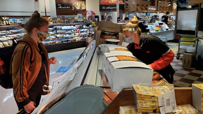 Une cliente devant un comptoir d'alimentation, derrière lequel une employée la sert.