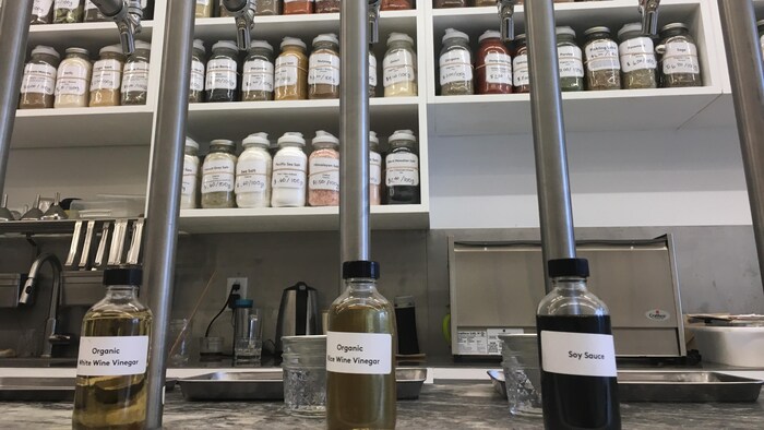 Des étagères avec des pots d'épices et trois distributeurs en fût à l'avant-plan avec trois bouteilles. 