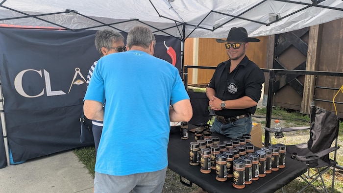 La personne derrière le kiosque sourit, alors que des clients magasinent des produits.