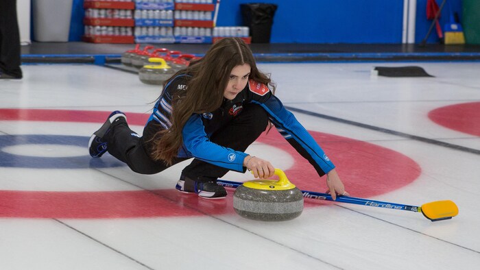 Une jeune femme lance une pierre de curling.