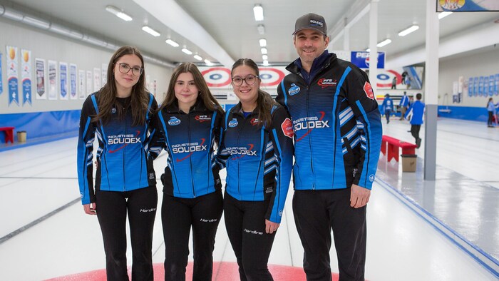 Quatre curleuses et leur entraîneur posent pour une photo sur la glace.