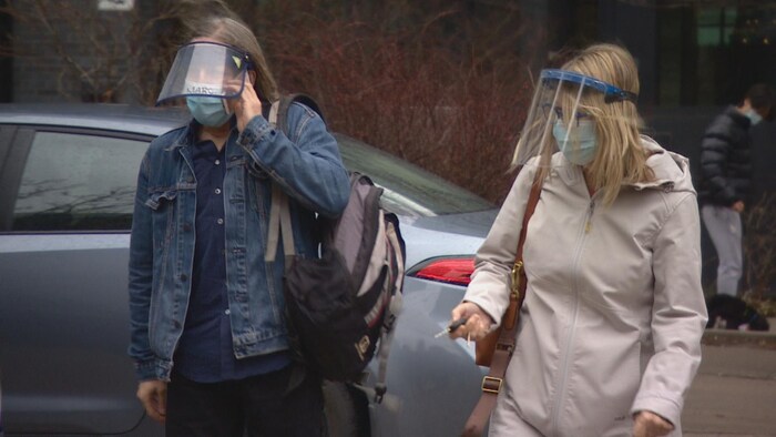 Un homme et une femme, portant des masques et visières, debout dans un stationnement.