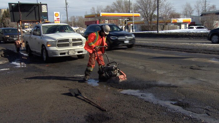 Un employé de la Ville en veston orange bouche des nids-de-poule.