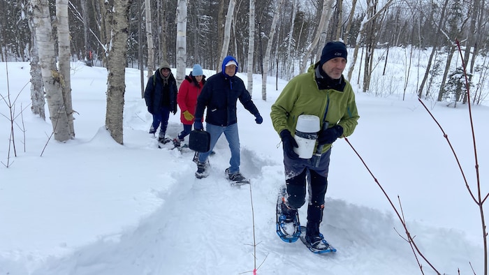 Sergio Rossi marche en raquette dans la forêt en transportant un pluviomètre.