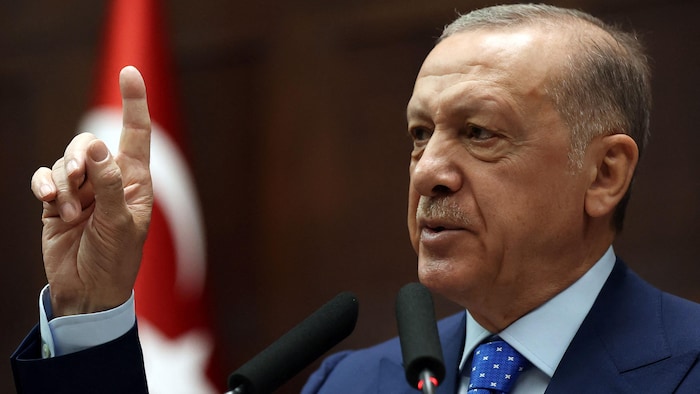 الرئيس التركي رجب طيّب أردوغان رافعاً سبابته اليمنى خلال إلقائه خطاباً، ويبدو العلم التركي في عمق الصورة.