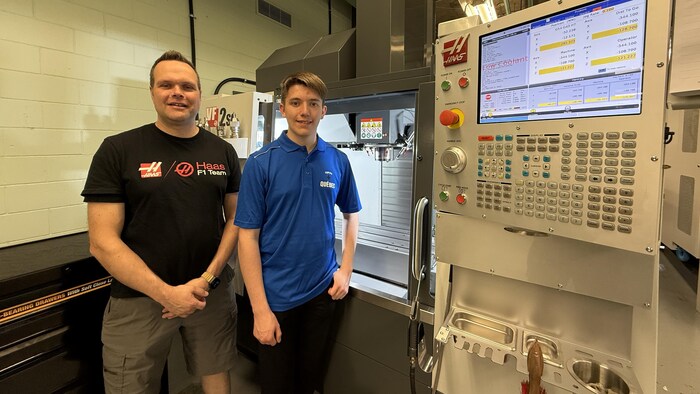 Deux hommes posent devant un centre d'usinage.
