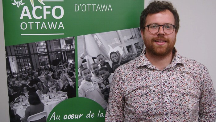 Éric Barrette devant une affiche de l'ACFO Ottawa.