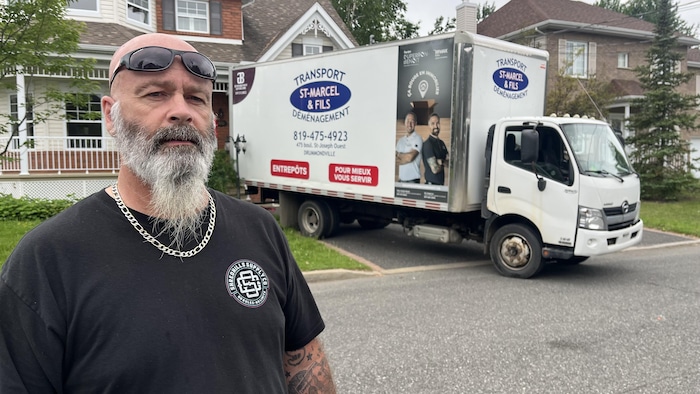 Un homme dans une rue devant une maison où un camion de déménagment est stationné.