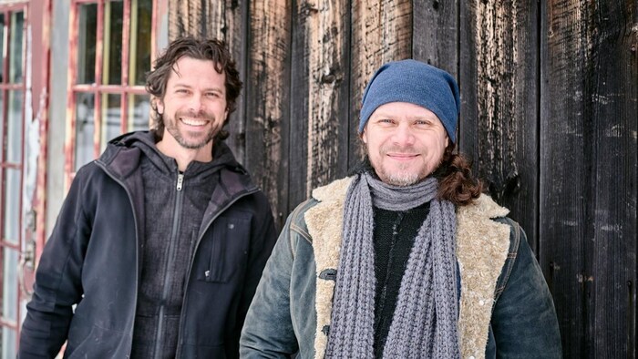 Les frères Simon et Éric Beaudry posent devant une grange, souriants.