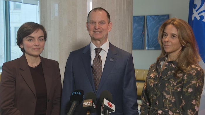 Trois personnes parlent derrière des micros et un drapeau du Québec.