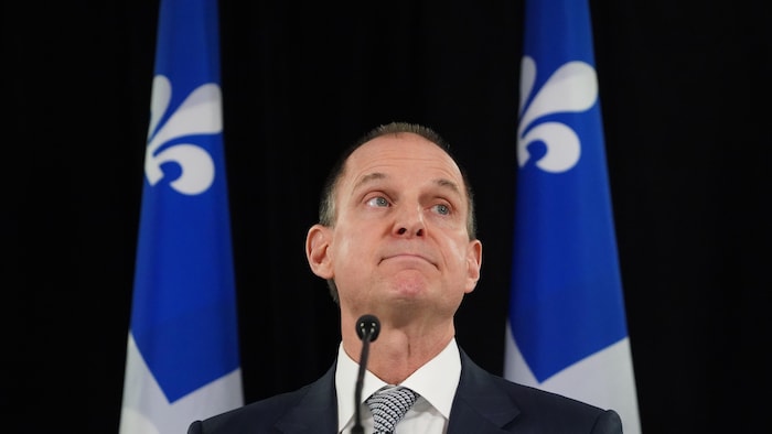 Eric Girard en conférence de presse, devant des drapeaux du Québec.