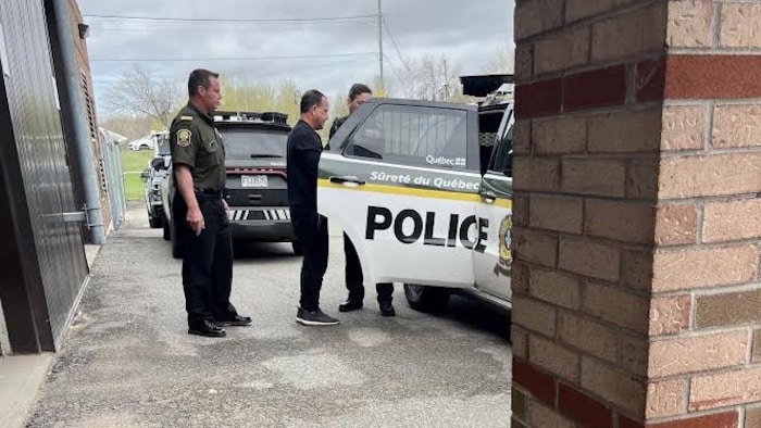 Un homme et deux policiers près d'une voiture de police.
