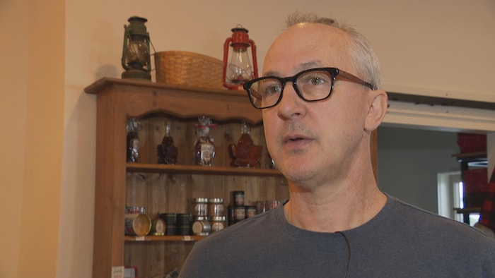 Éric Haché en entrevue, des produits d'érable sur des étagères derrière lui.
