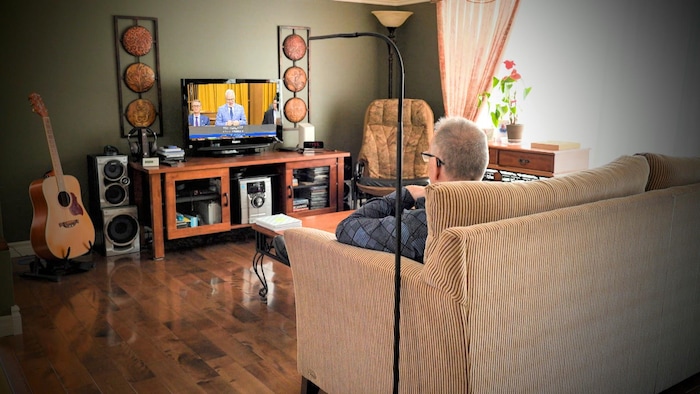 Martial Lavoie regarde la télévision, assis dans sa salle de séjour.