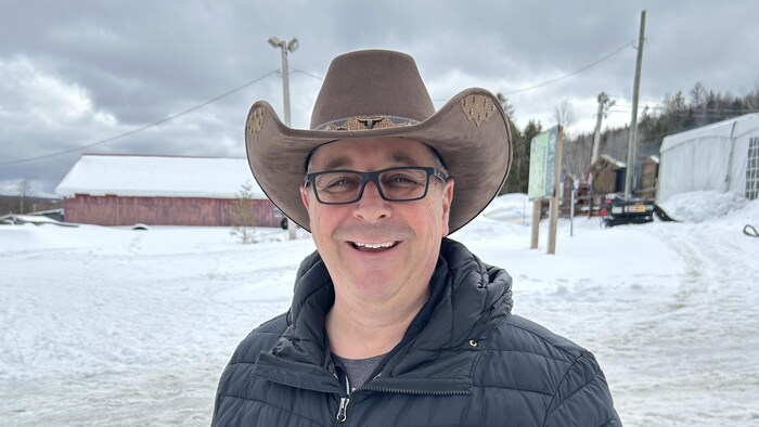 Le maire coiffé d'un chapeau de cowboy est debout dans la neige et sourit en regardant le photographe.