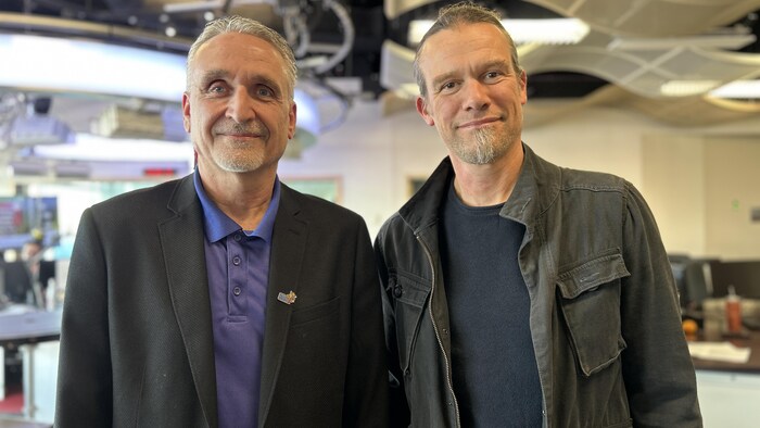 Deux hommes aux cheveux poivre et sel regardent la caméra dans notre studio. Il sourient.