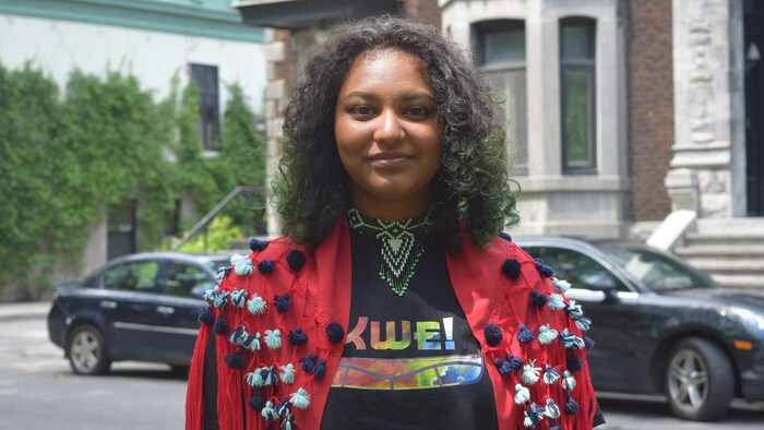Une jeune femme se tient debout à l'extérieur et regarde la caméra.