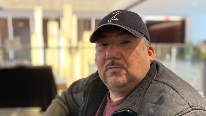 Ernest Tomatuk fixe l'objectif, assis dans le lobby d'un hôtel.
