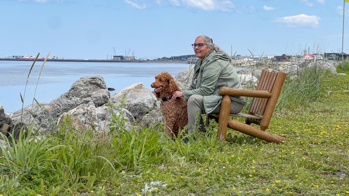 Marie-Sylvie Bénard est assise avec son caniche sur le bord du fleuve.