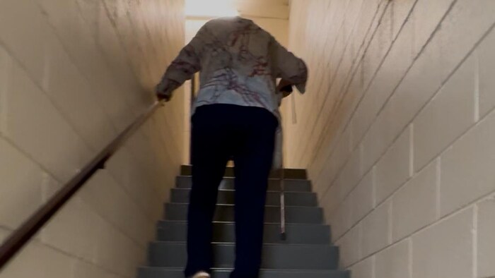 Une personne âgée monte les escaliers en tenant sa canne