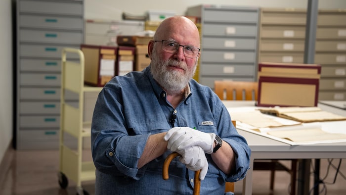Frank Mackey assis à un bureau où se trouvent des archives.