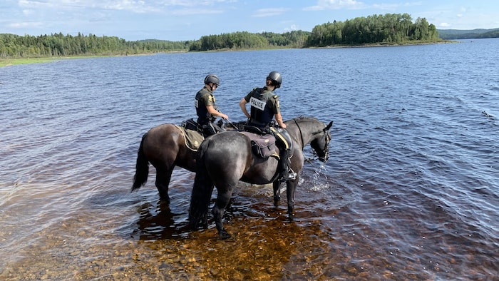 Deux policières de la SQ à dos de leur cheval prennent une pause dans un lac.