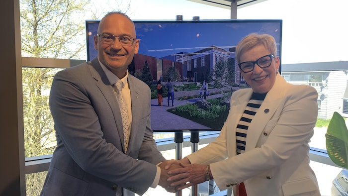 Sébastien D'Astous et Suzanne Blais joignent leurs mains en souriant pour la caméra, devant une esquisse.