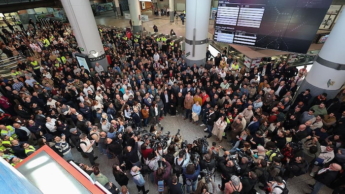 Des centaines de voyageurs regroupés debout, immobiles,  se recueillent pour une minute de silence en mémoire des victimes de la catastrophe ferroviaire.