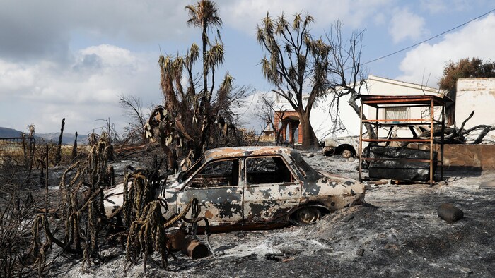 Une voiture calcinée devant une maison endommagée par le feu.
