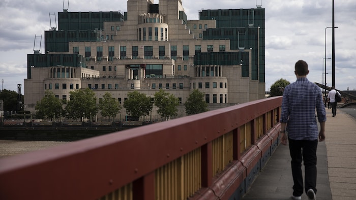 Un homme marche sur un pont avec la bâtisse en arrière-plan.