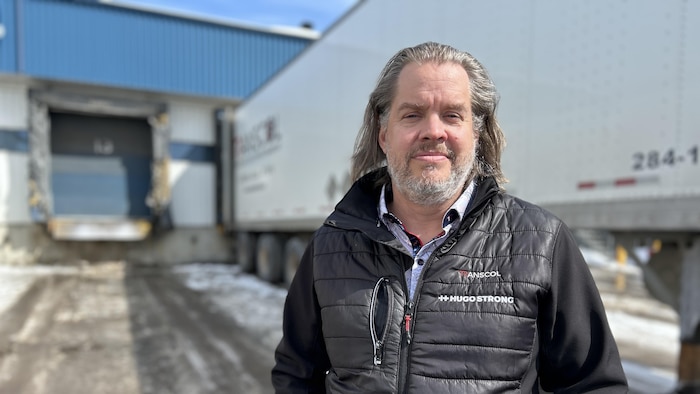 Un homme situé devant un camion prend la pose en hiver avec les deux mains dans les poches de son pantalon.